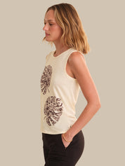 Woman wearing a cream sleeveless top with leaf pattern on a plain background