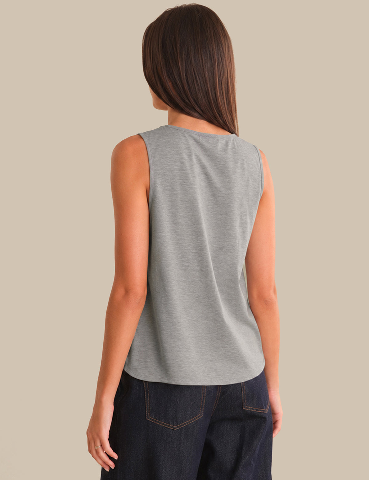 Person wearing a gray sleeveless top and dark jeans on a beige background