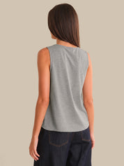 Person wearing a gray sleeveless top and dark jeans on a beige background