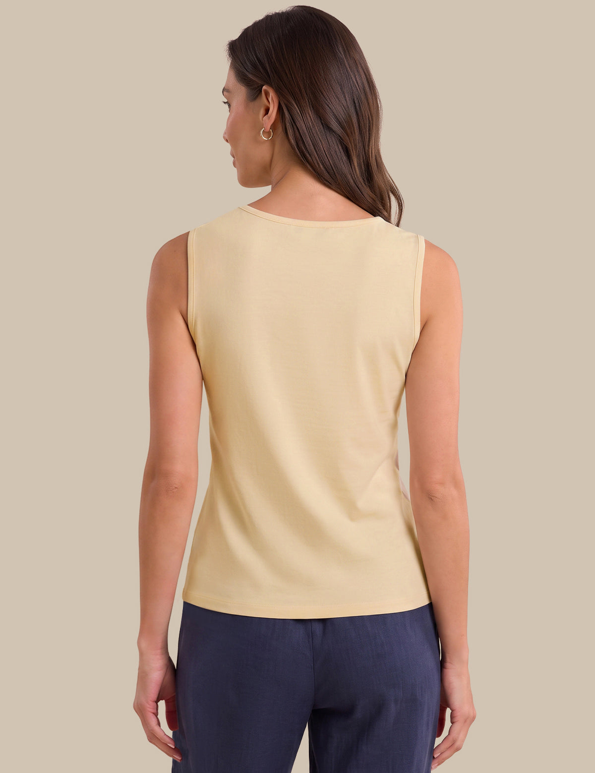 A woman shown from the back wearing a sleeveless cream-colored top and navy blue pants, set against a solid beige background.