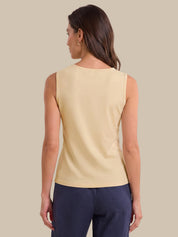 A woman shown from the back wearing a sleeveless cream-colored top and navy blue pants, set against a solid beige background.
