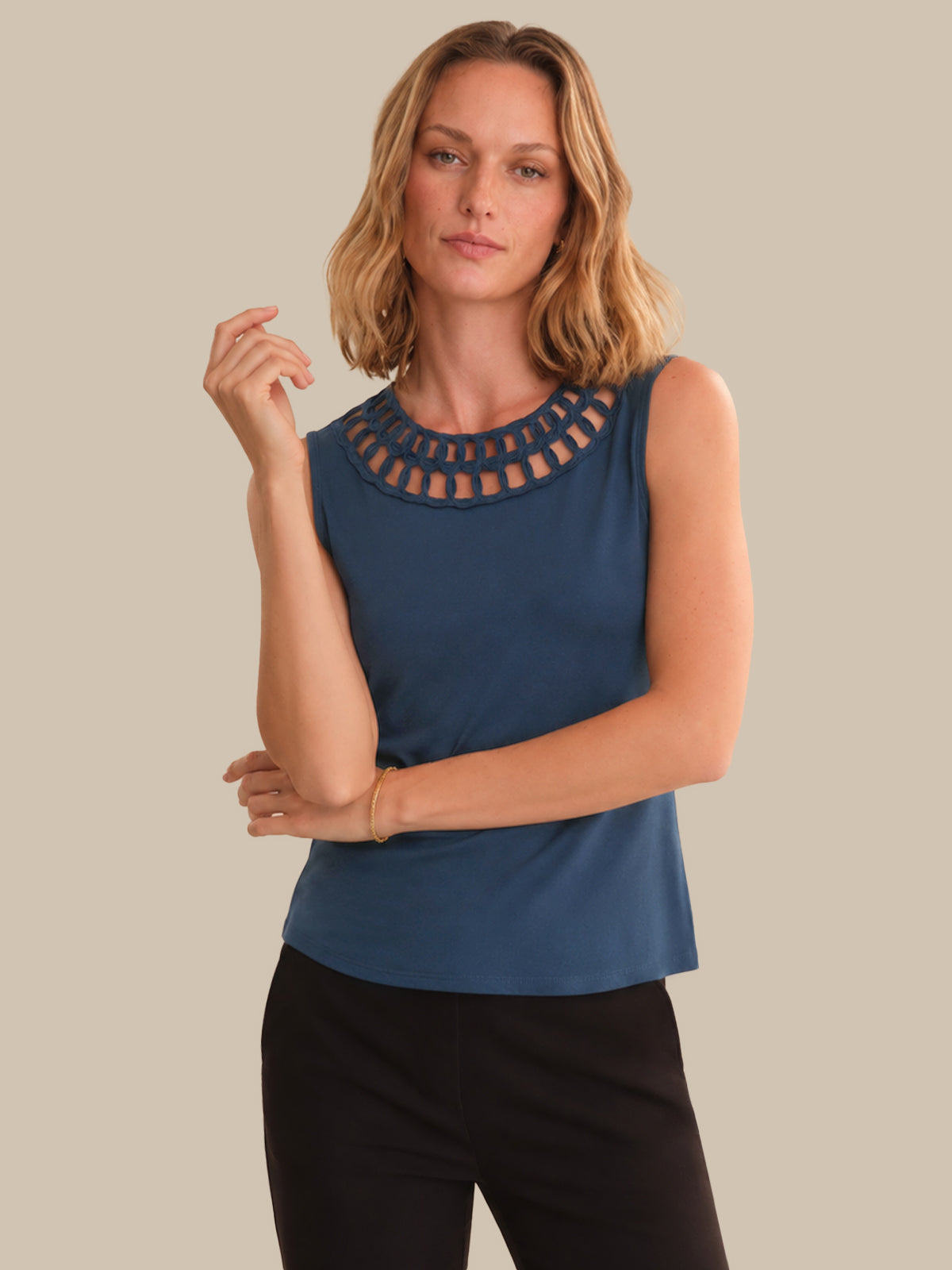 Woman wearing a blue sleeveless top with cut-out details on a beige background