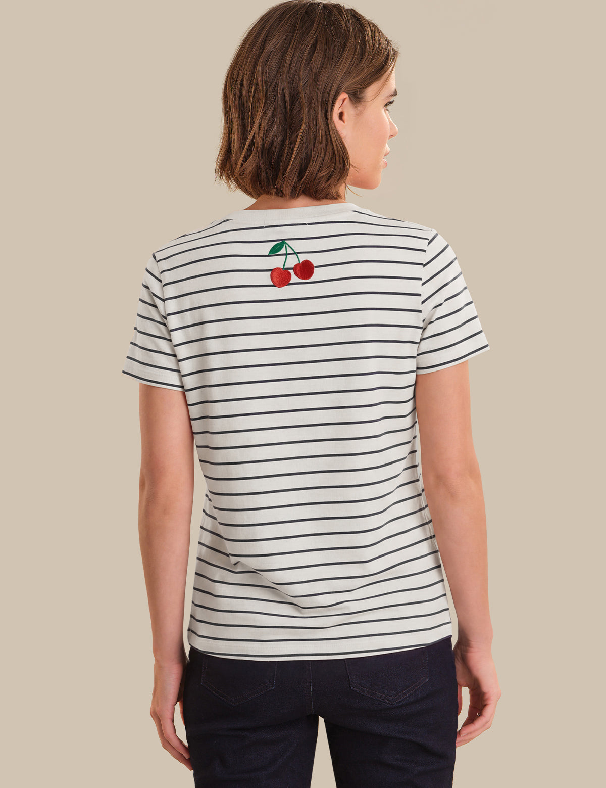 Person wearing a striped t-shirt with cherry design on the back against a beige background