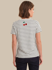 Person wearing a striped t-shirt with cherry design on the back against a beige background