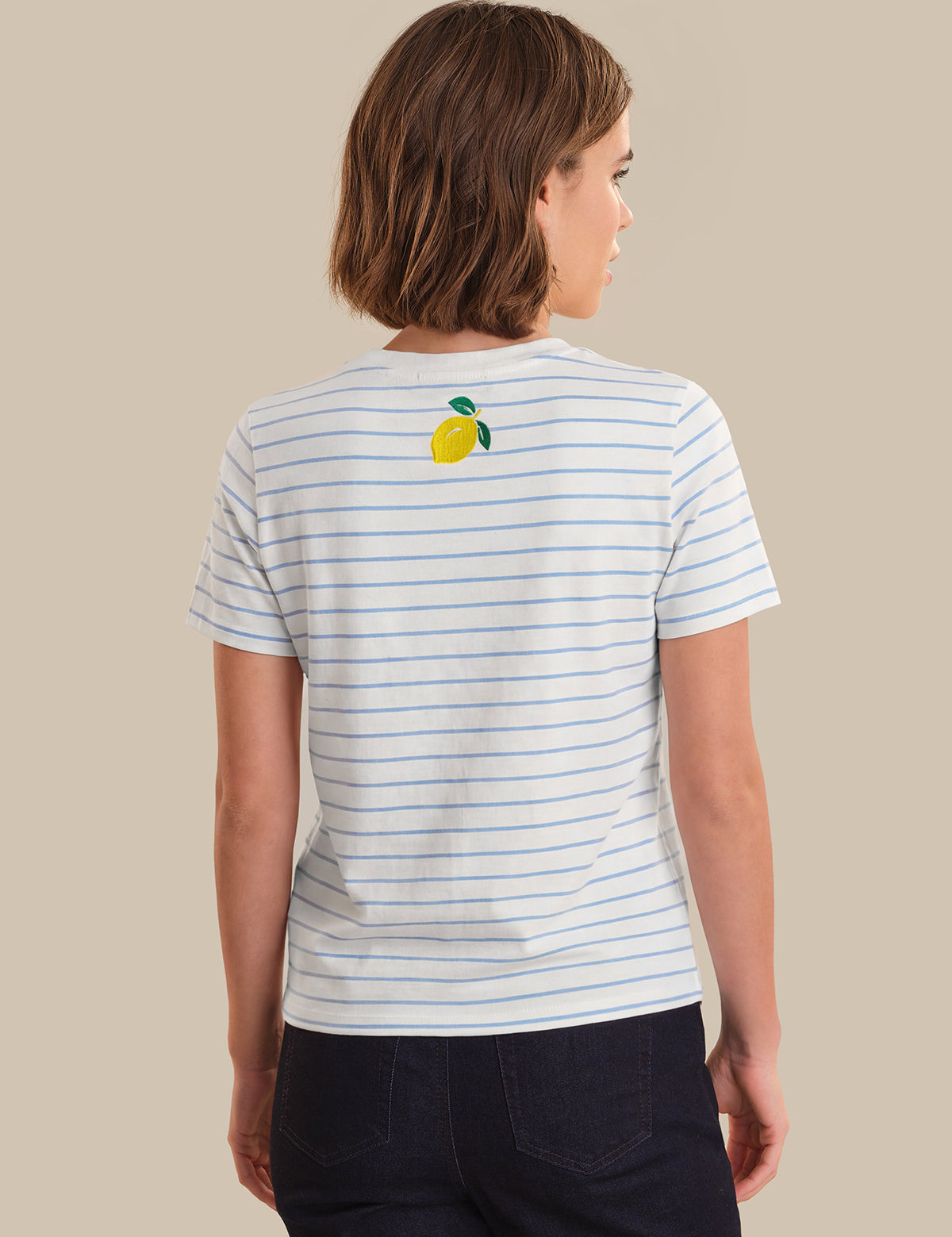 Person wearing a striped t-shirt with a lemon graphic on the back against a beige background