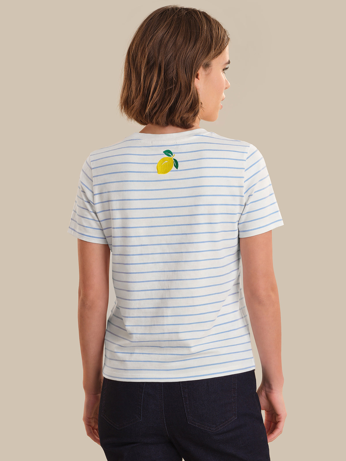 Person wearing a striped t-shirt with a lemon graphic on the back against a beige background