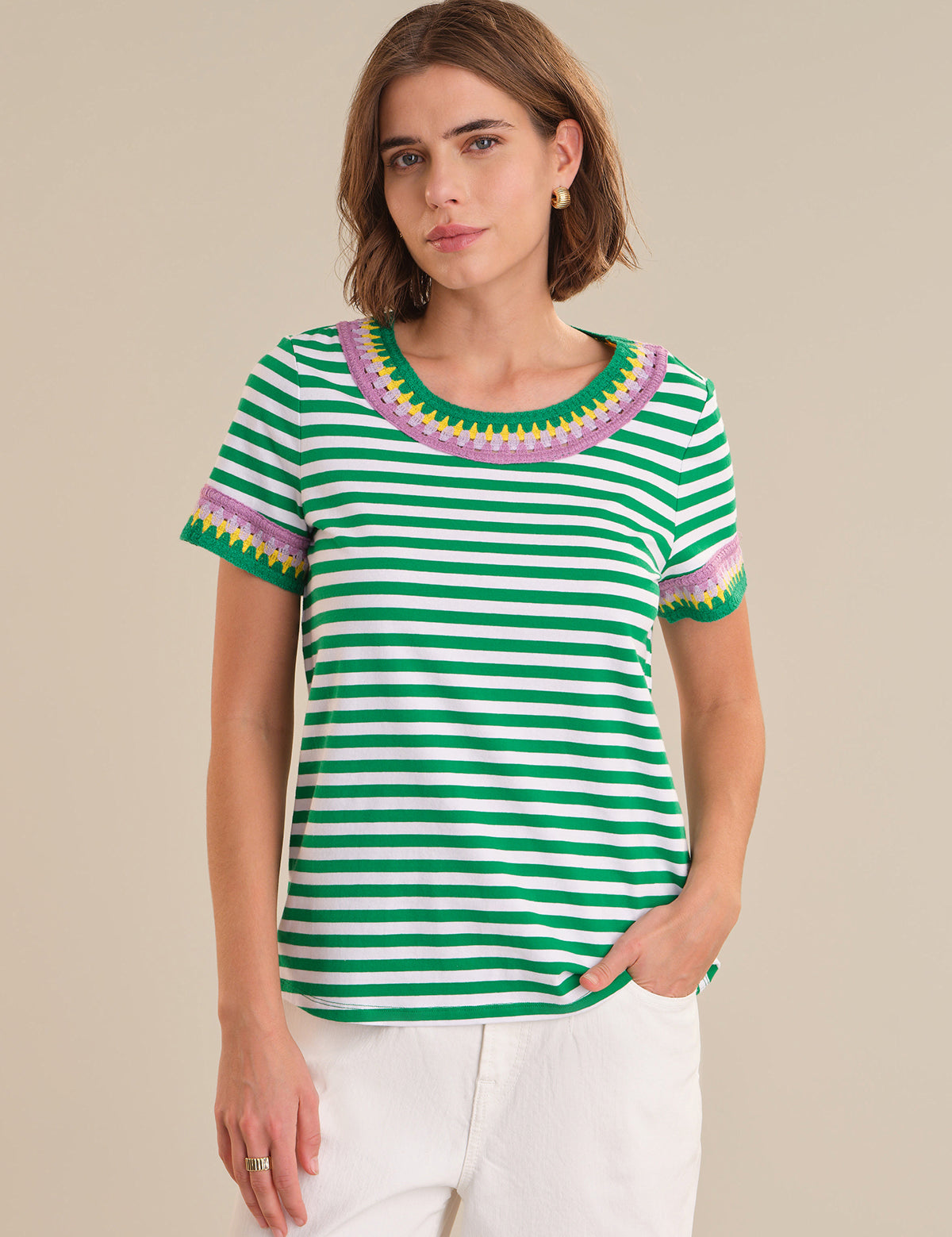 Woman wearing a green and white striped shirt with colorful trim on a beige background