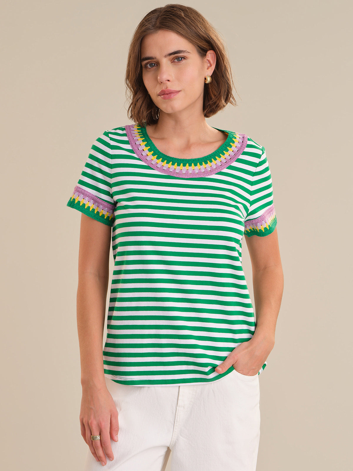Woman wearing a green and white striped shirt with colorful trim on a beige background