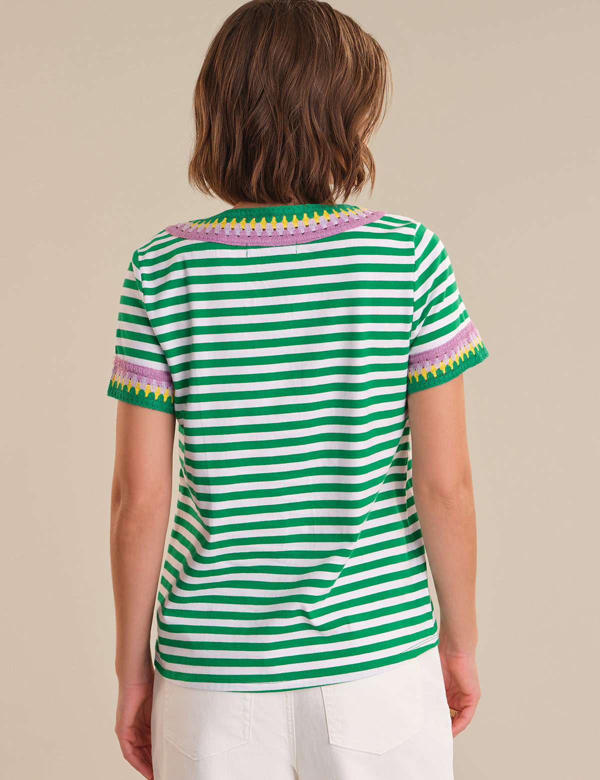 Person wearing a green and white striped shirt with colorful trim on a beige background