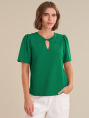 Woman wearing a green blouse with a cut-out detail on a beige background