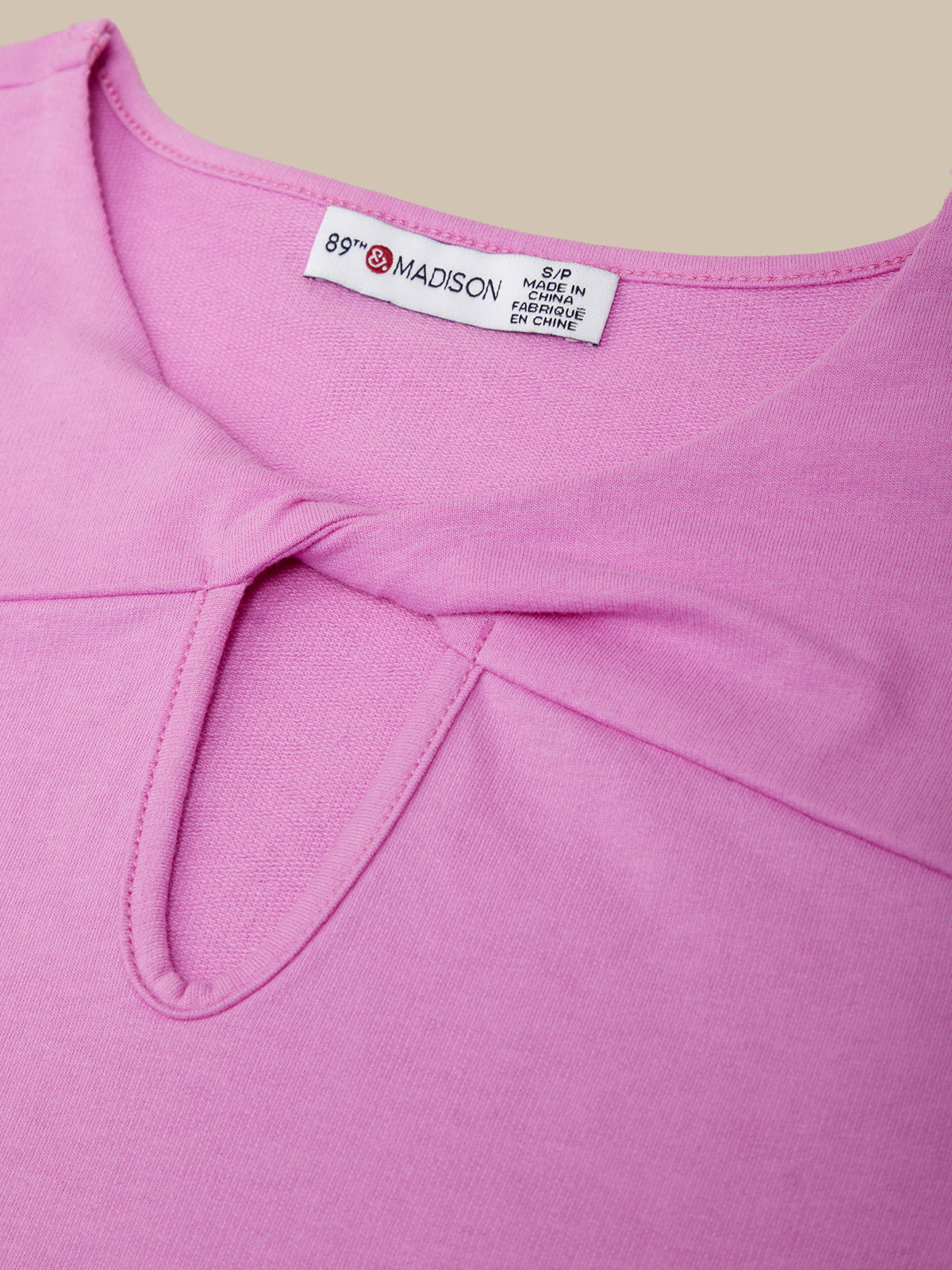Close-up of a pink garment with a brand label on a beige background