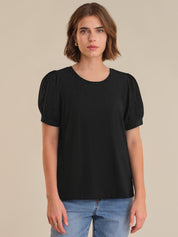 Woman wearing a black top with puff sleeves against a beige background