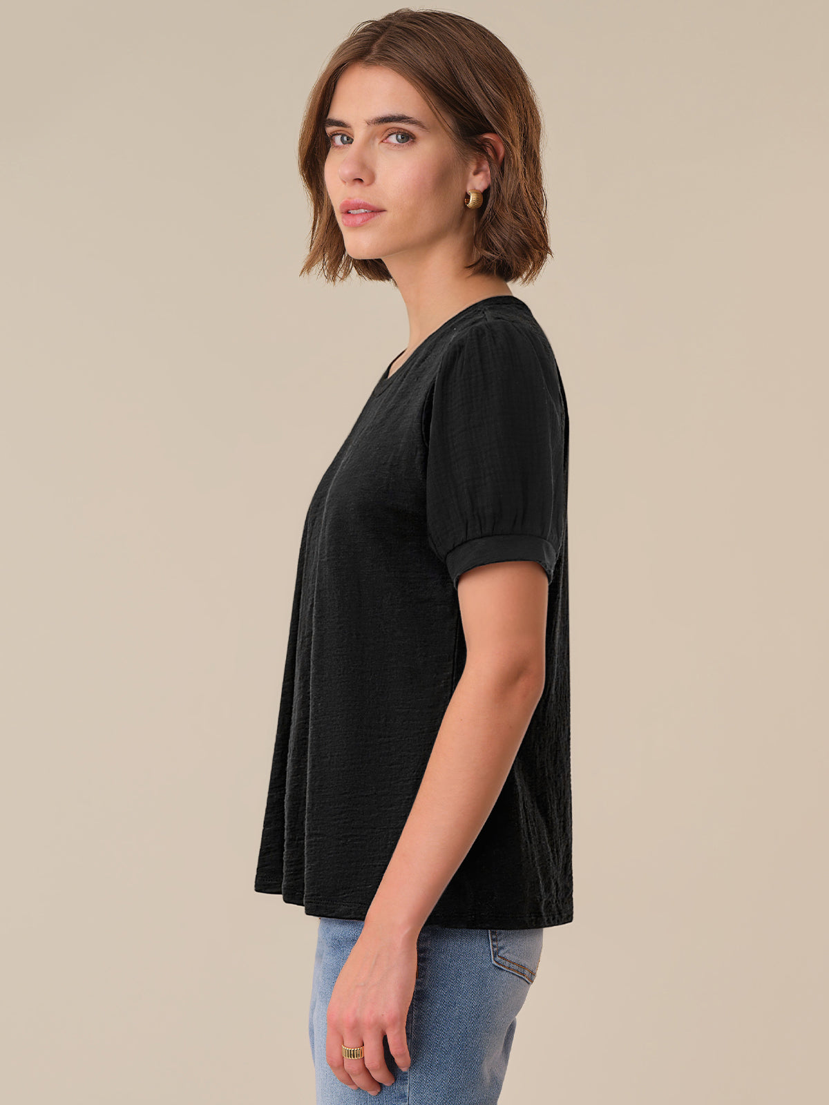 Woman wearing a black top and blue jeans against a beige background