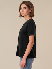 Woman wearing a black top and blue jeans against a beige background