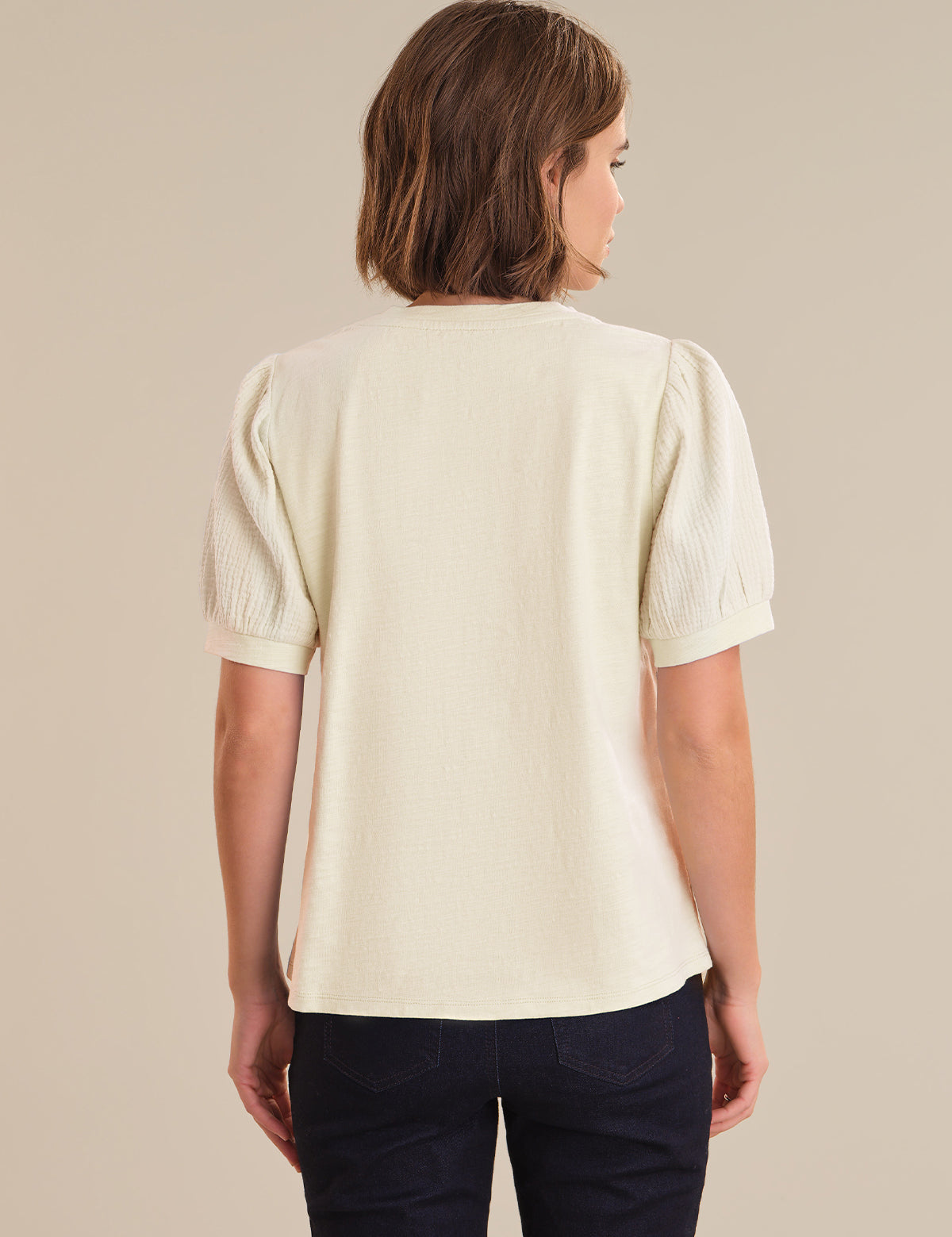 Woman wearing a light-colored blouse with puff sleeves against a beige background