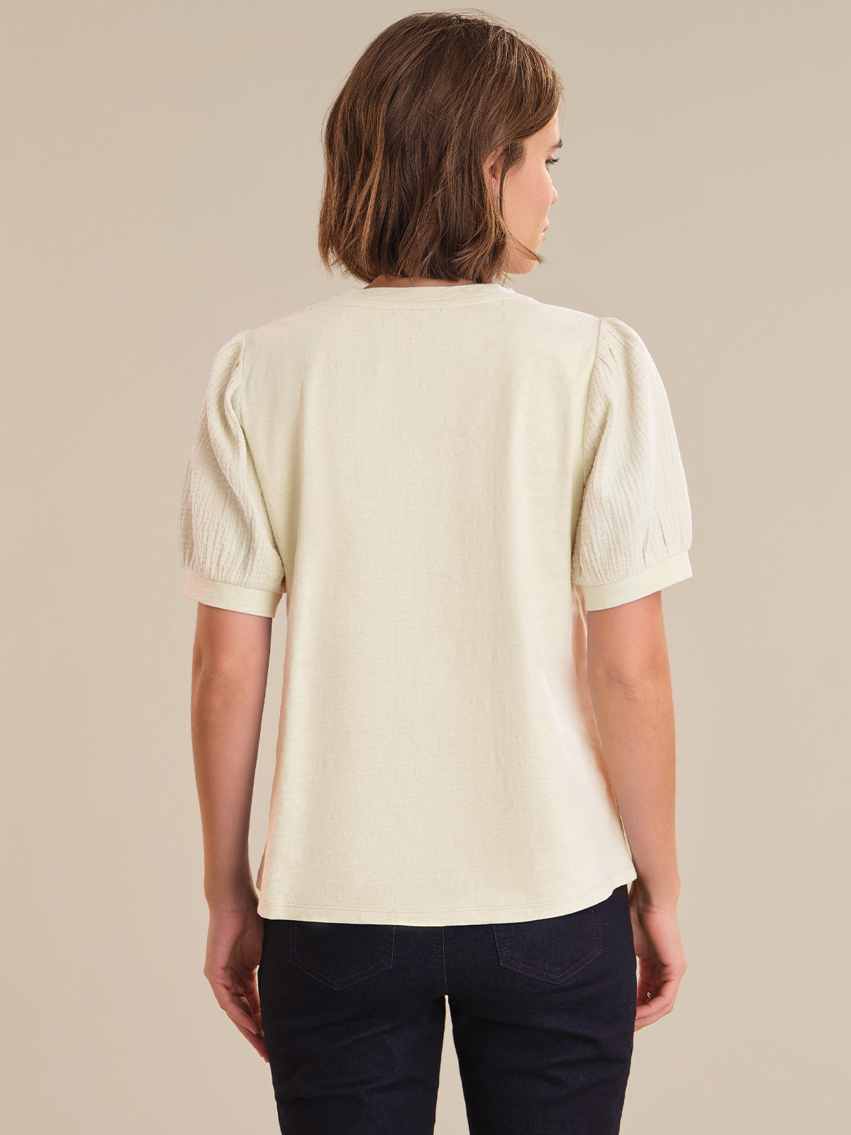 Woman wearing a light-colored blouse with puff sleeves against a beige background