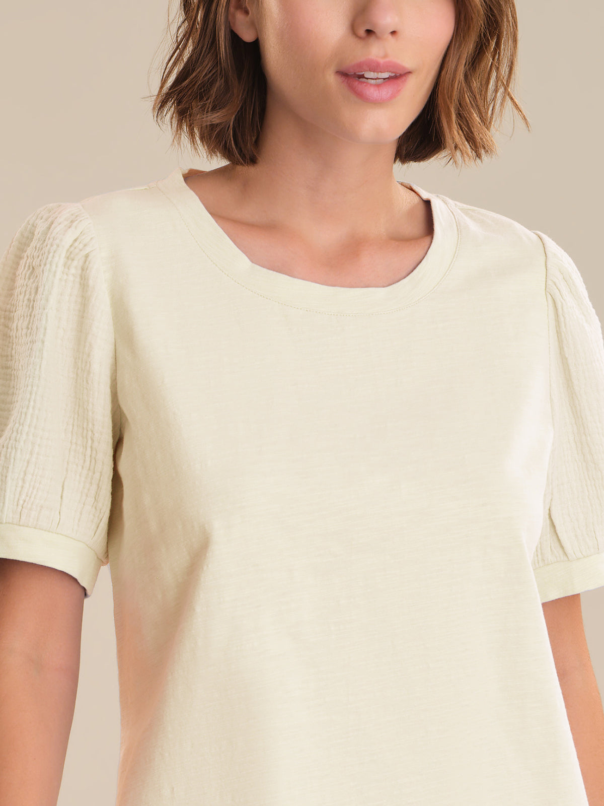 Woman wearing a light-colored blouse with short sleeves against a neutral background