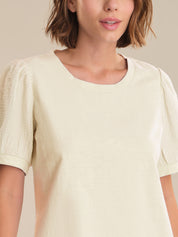 Woman wearing a light-colored blouse with short sleeves against a neutral background