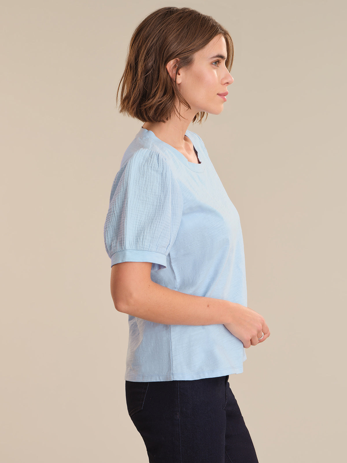 Woman wearing a light blue top and dark pants on a beige background