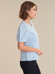 Woman wearing a light blue top and dark pants on a beige background