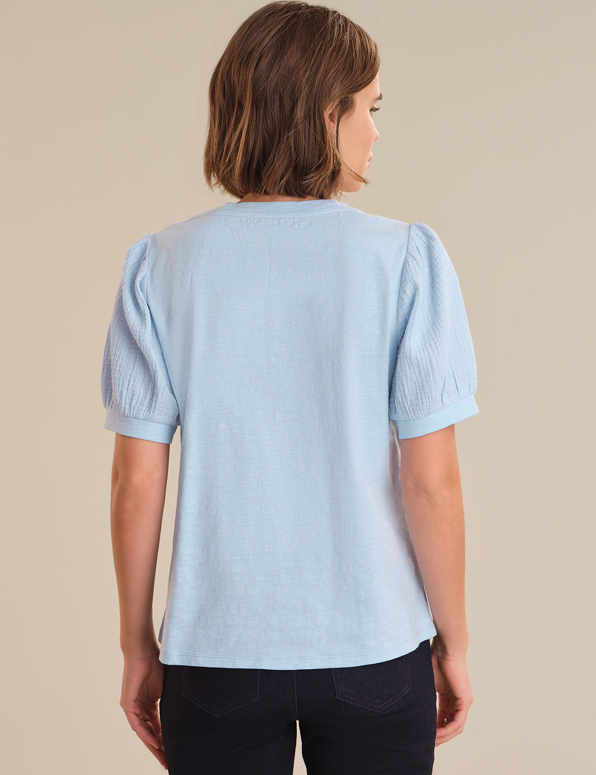 Woman wearing a light blue blouse with puffed sleeves on a beige background