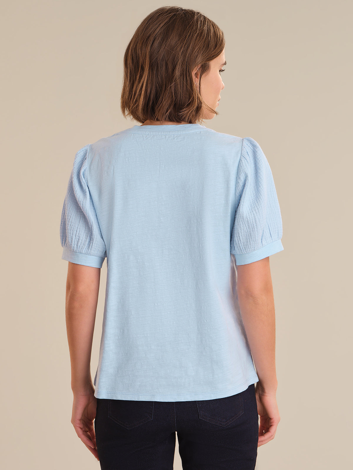 Woman wearing a light blue blouse with puffed sleeves on a beige background