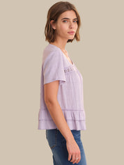 Woman wearing a light purple layered top against a beige background