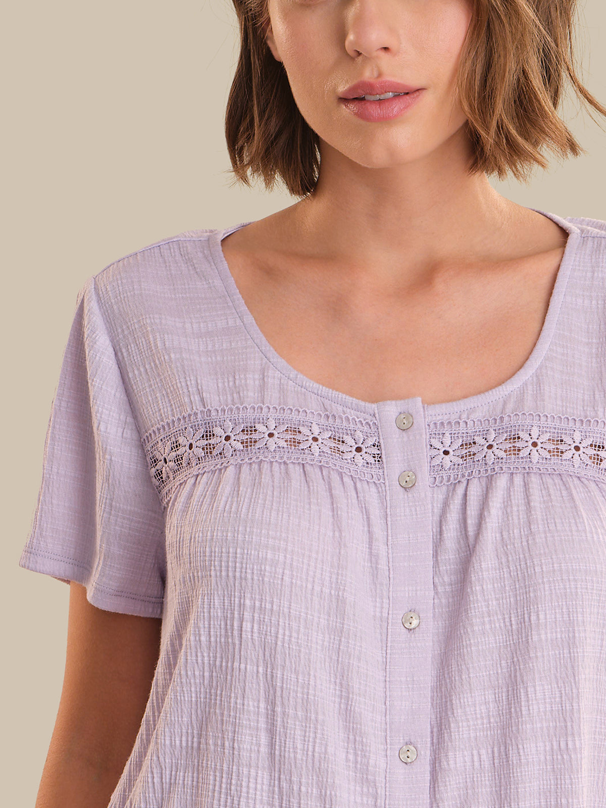 Woman wearing a light purple blouse with lace details on a beige background