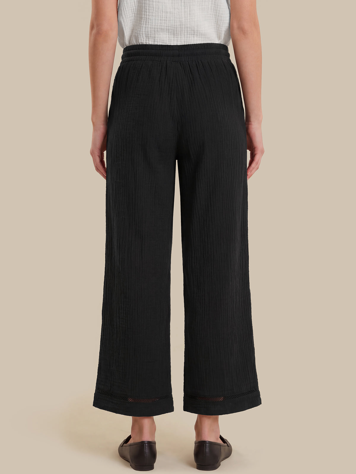 Person wearing black wide-leg pants on a beige background