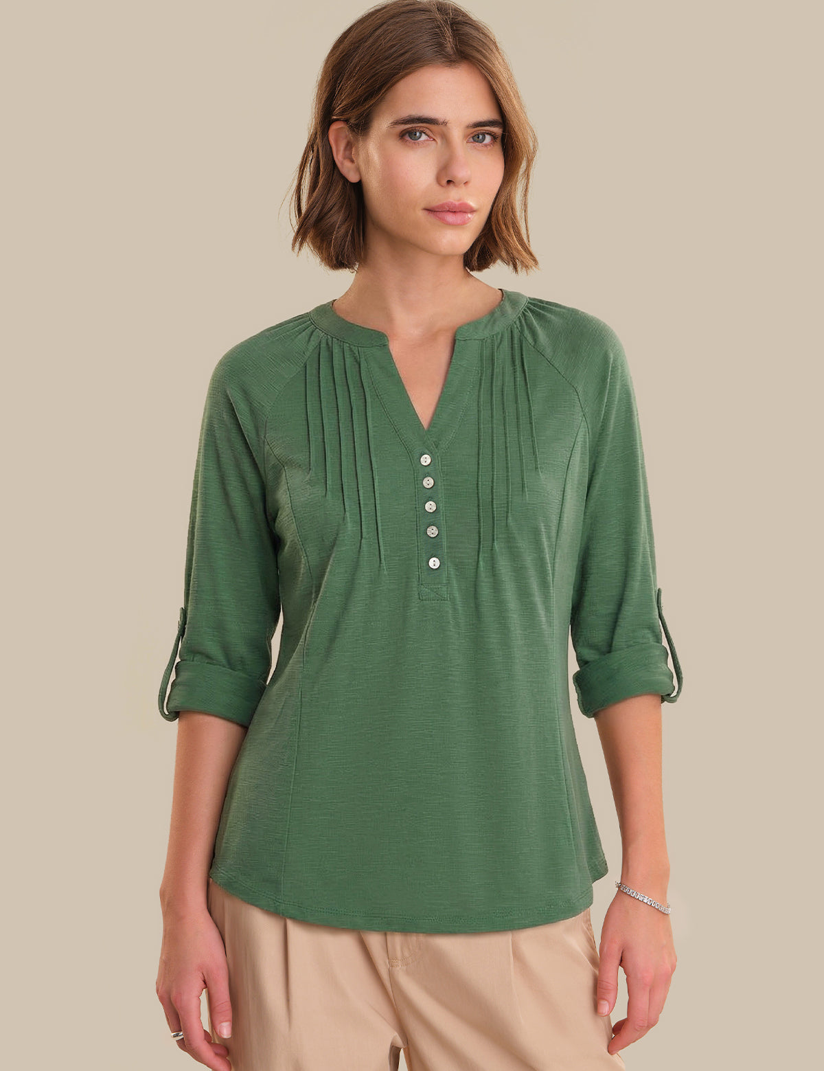 Woman wearing a green blouse with rolled-up sleeves on a beige background