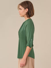 Woman wearing a green top with rolled-up sleeves against a beige background