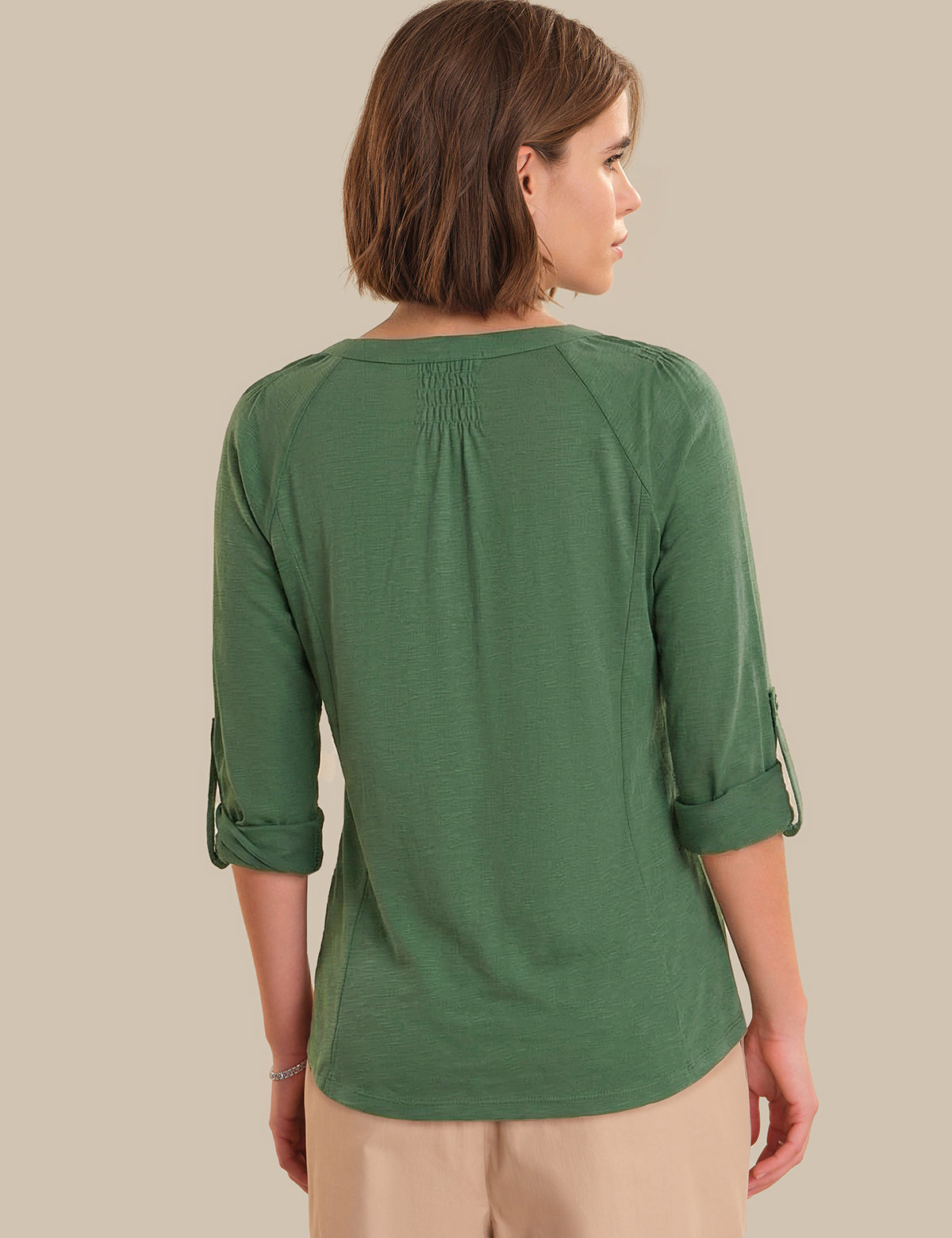Woman wearing a green top with rolled-up sleeves on a beige background
