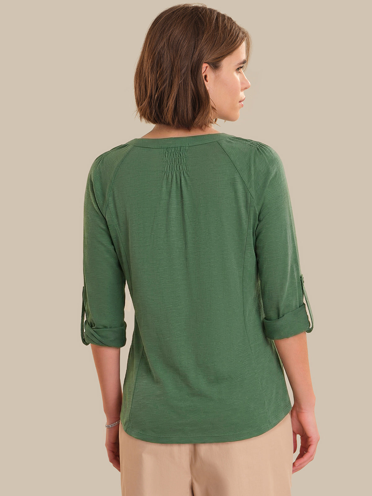 Woman wearing a green top with rolled-up sleeves on a beige background