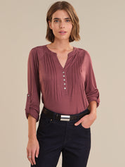 Woman wearing a maroon long-sleeve top with buttons and dark pants on a beige background