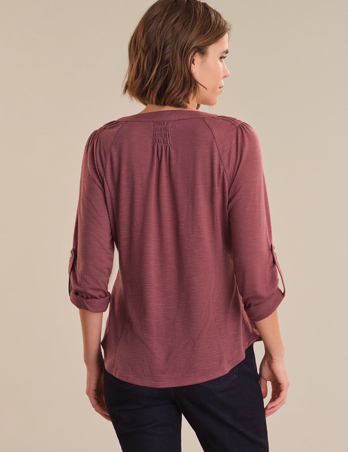 Woman wearing a mauve long-sleeve top with rolled-up sleeves on a beige background