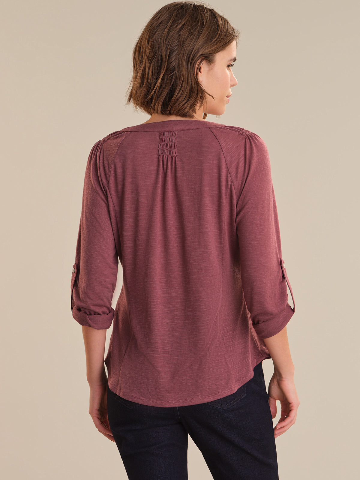 Woman wearing a mauve long-sleeve top with rolled-up sleeves on a beige background