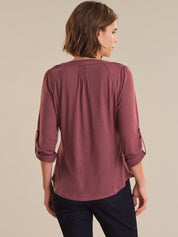 Woman wearing a mauve long-sleeve top with rolled-up sleeves on a beige background