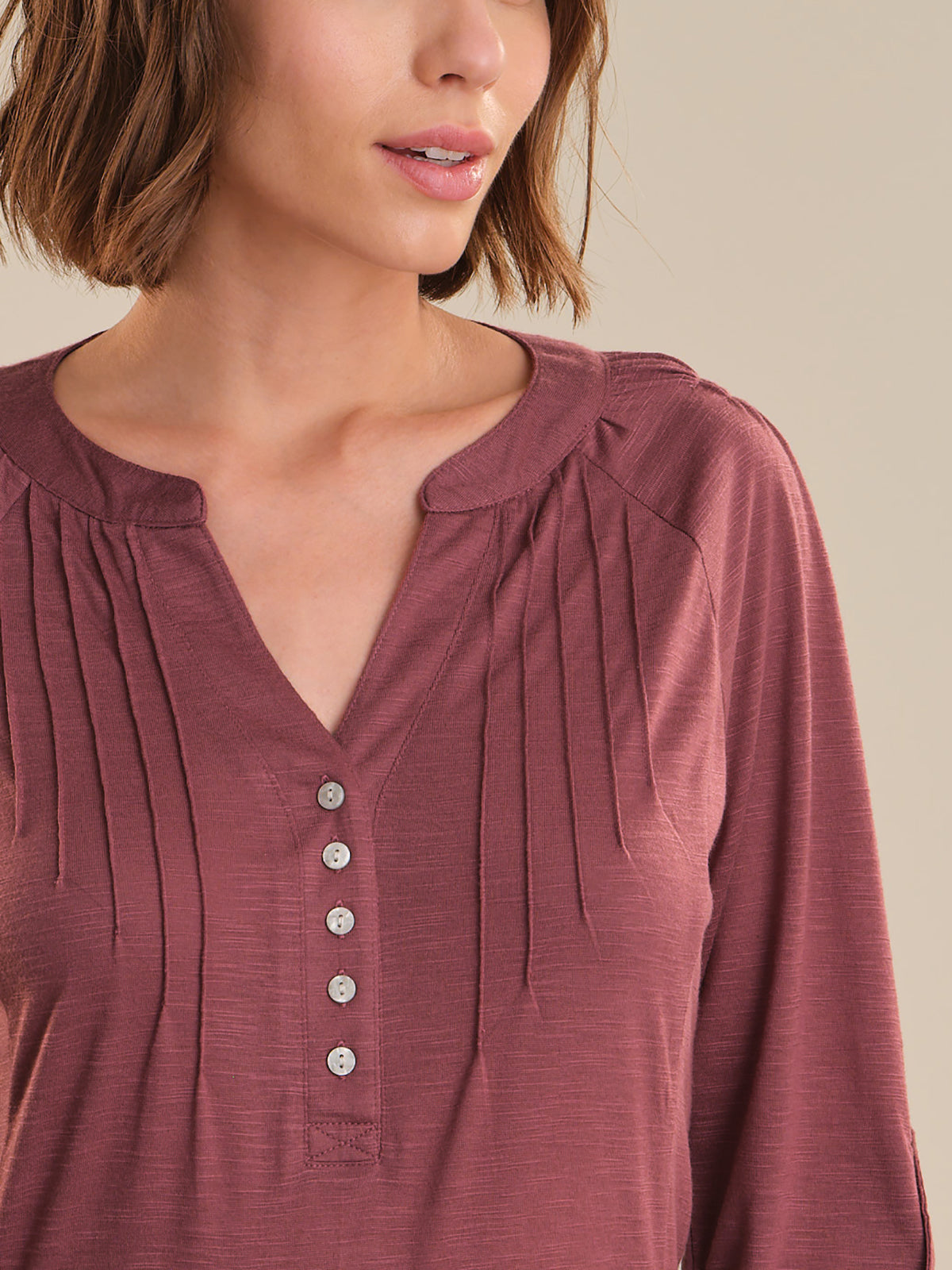 Close-up of a woman wearing a maroon long-sleeve top with button details on a neutral background