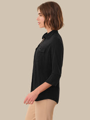 Woman wearing a black shirt and beige pants against a beige background