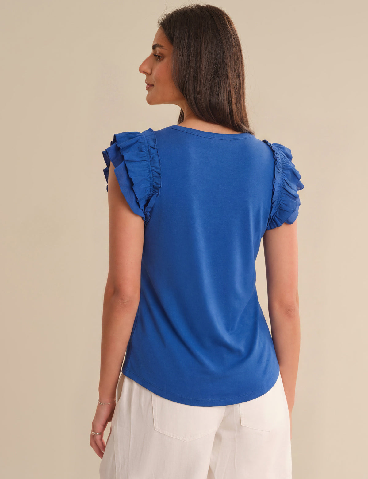 Woman wearing a blue top with ruffled sleeves on a beige background