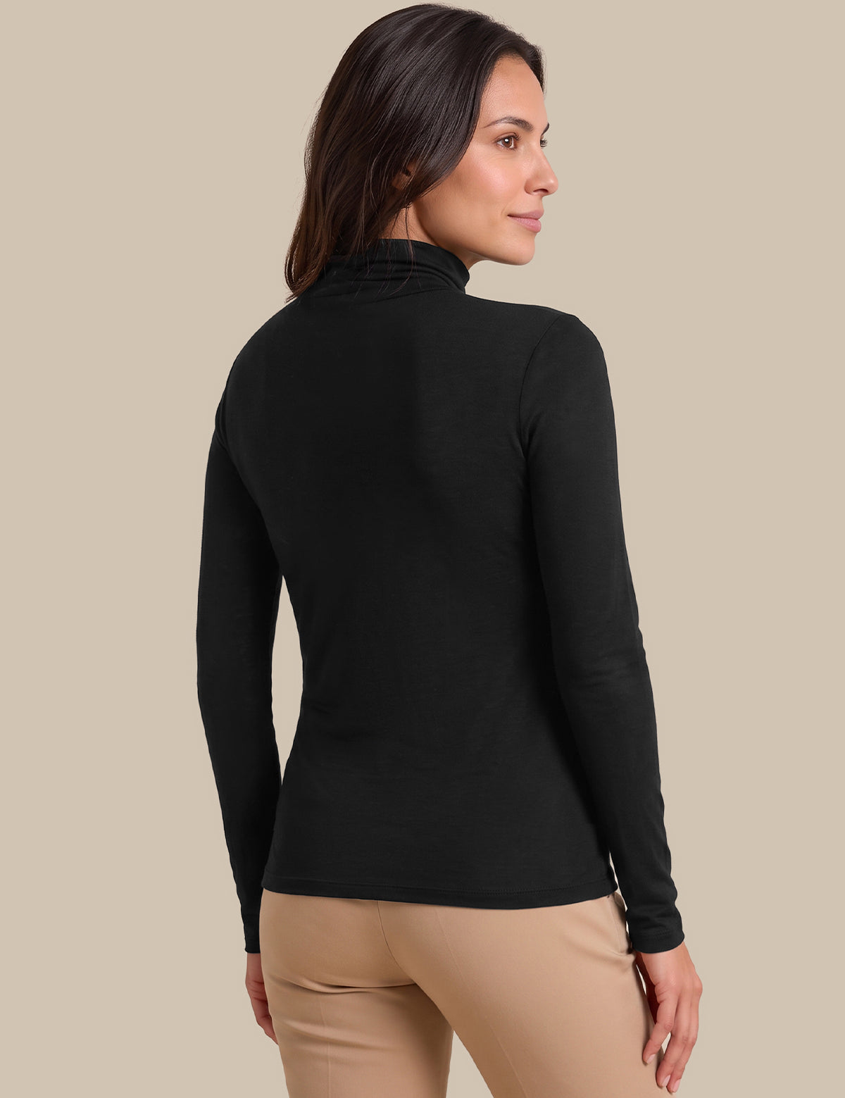 A woman shown from the back wearing a fitted black long-sleeve mock neck top and beige pants, against a plain beige studio background.