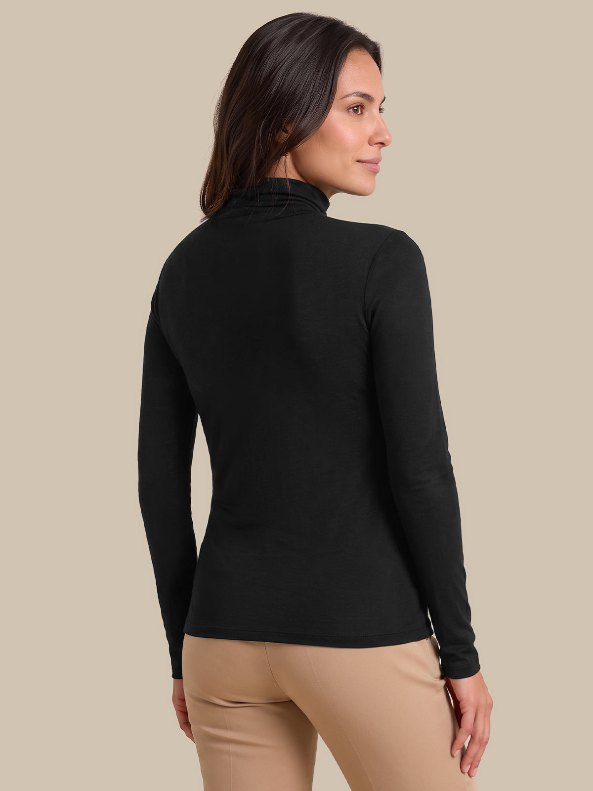 A woman shown from the back wearing a fitted black long-sleeve mock neck top and beige pants, against a plain beige studio background.