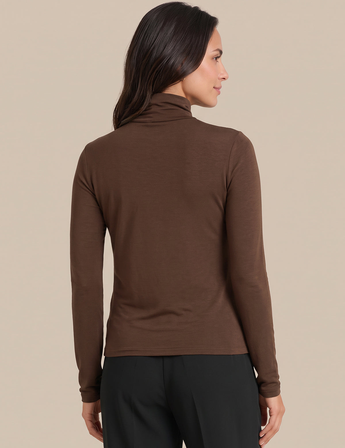 A woman shown from the back wearing a fitted brown long-sleeve turtleneck top and black pants against a plain beige studio background.