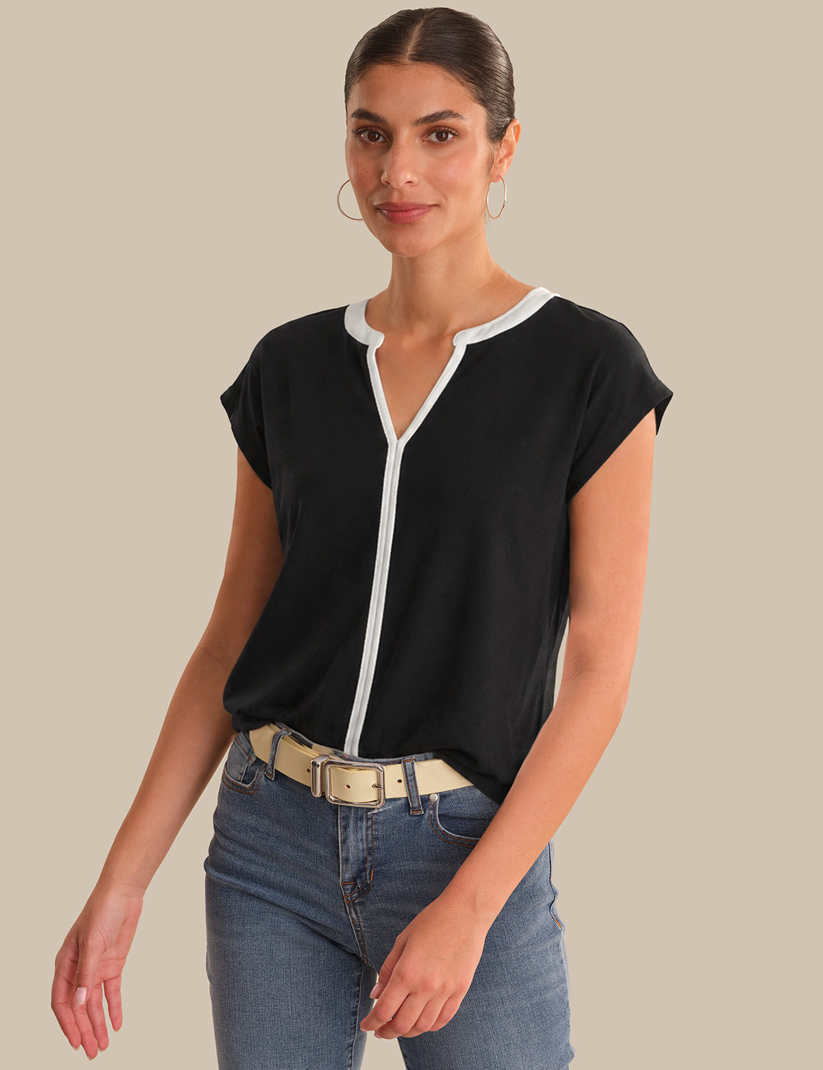 Woman wearing a black top with a white zipper and blue jeans on a beige background