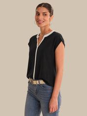 Woman wearing a black top with white trim and blue jeans on a beige background