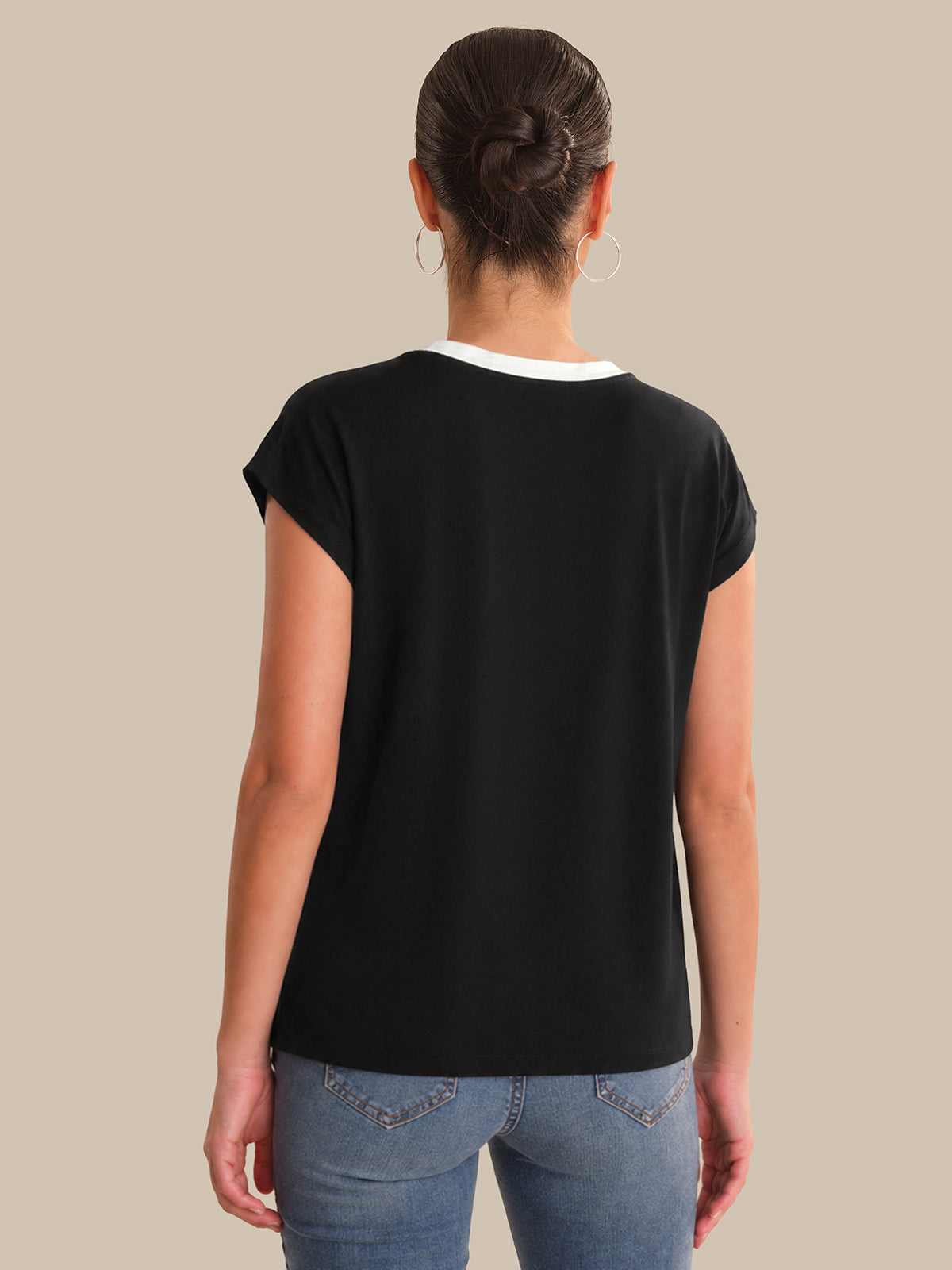 Person wearing a black t-shirt and blue jeans on a beige background