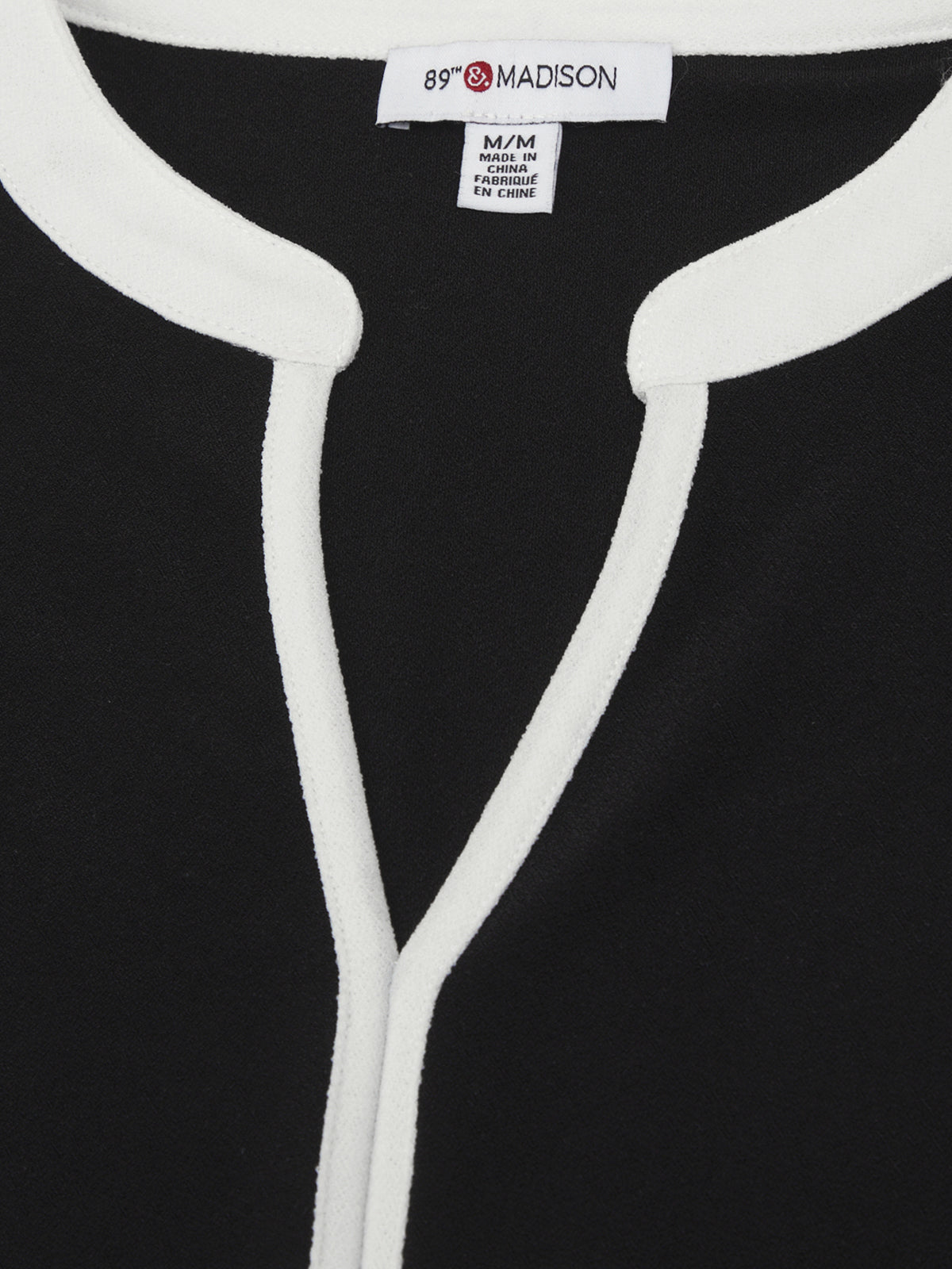 Close-up of a black garment with white piping and a visible label.