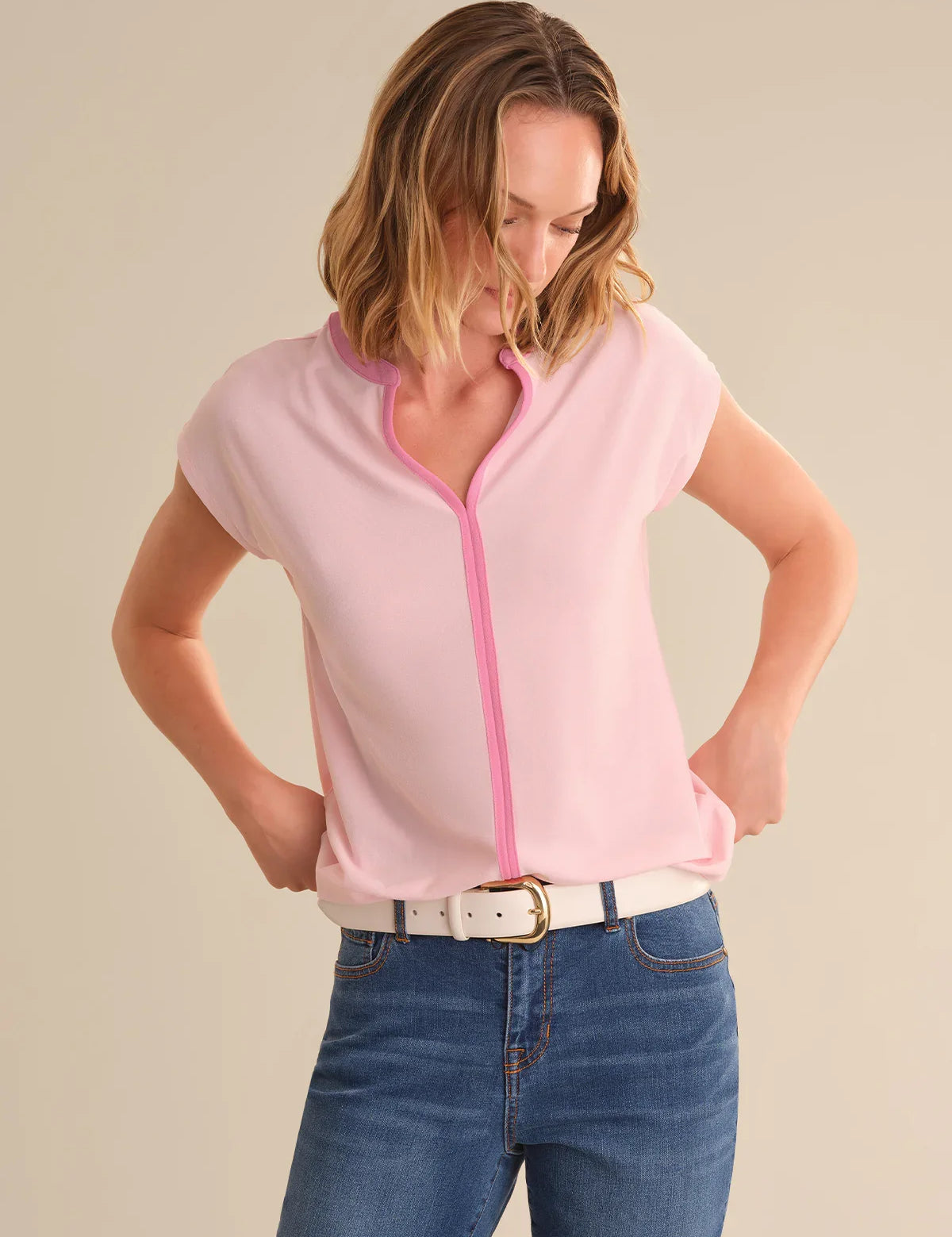 Woman wearing a pink tipped top with blue jeans on a beige background