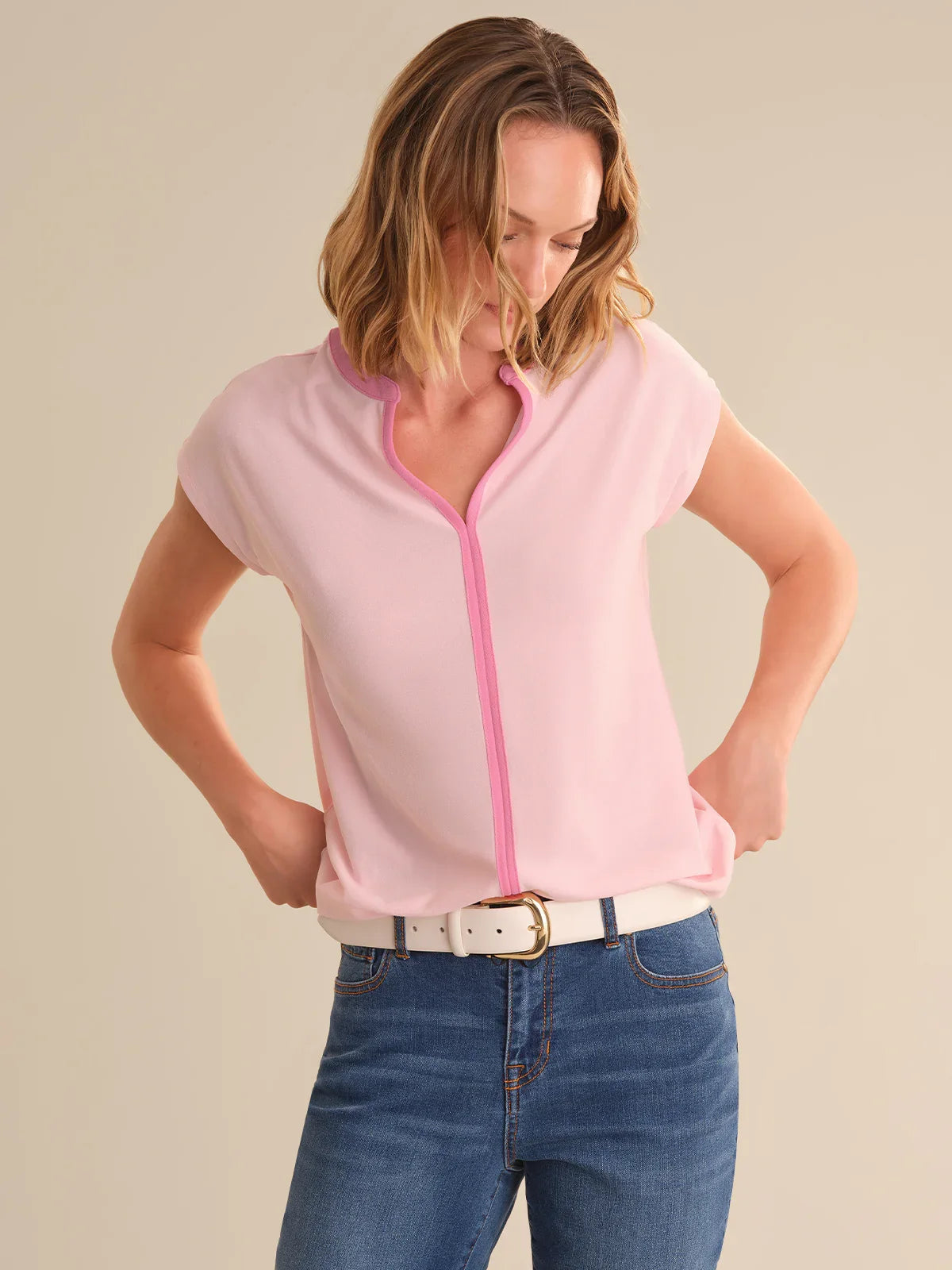 Woman wearing a pink tipped top with blue jeans on a beige background