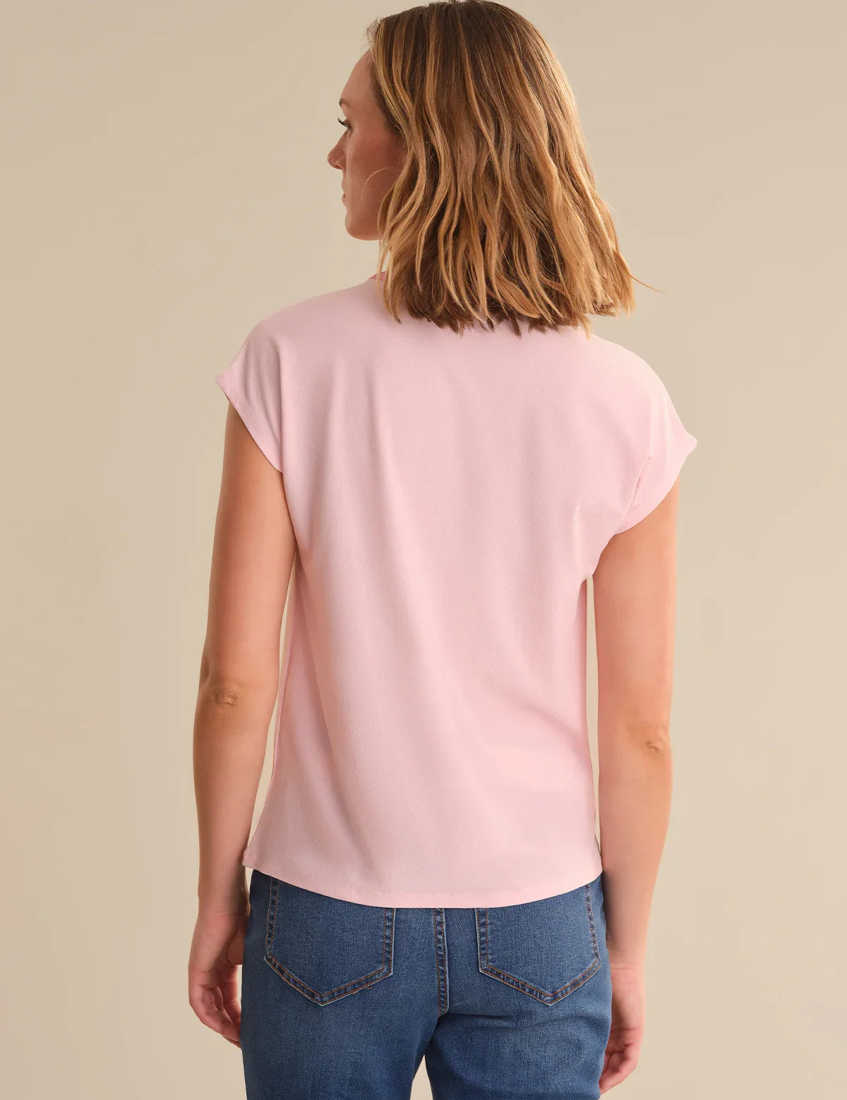 Woman wearing a pink t-shirt and blue jeans on a beige background